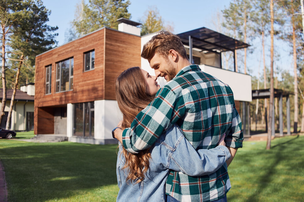 Ein junges heterosexuelles Pärchen steht vor einem neu erbauten Haus.