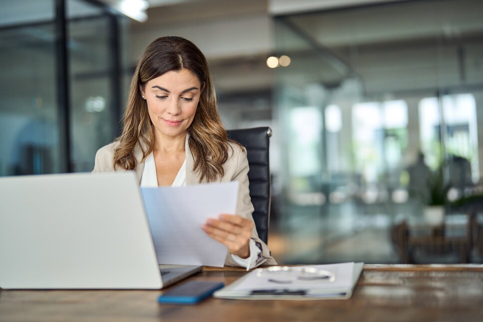Eine junge Frau sitzt im Business-Outfit vor einem Laptop. 