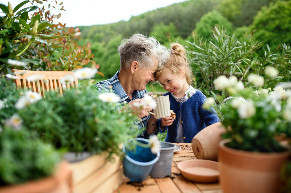 Eine ältere Dame sitzt mit einem jungen Kind - ihrer Enkelin - am Gartentisch.