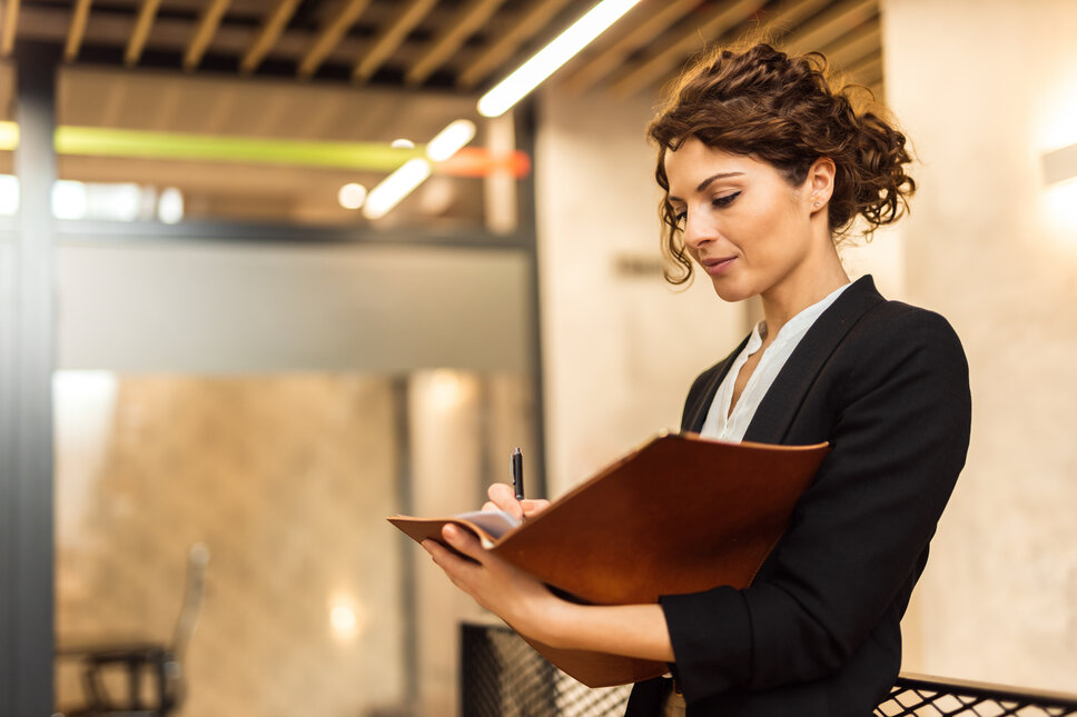 Eine junge Business-Frau steht im Büro und liest in einer Akte. 